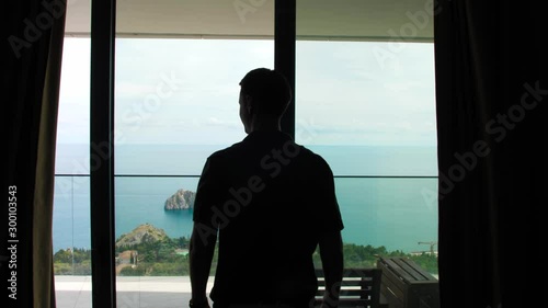 couple in hotel room by the sea, man opens curtains, hugging at the window