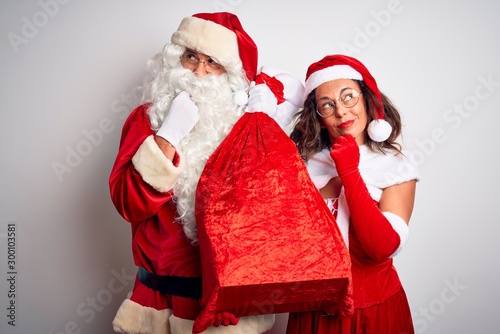 Senior couple wearing Santa Claus costume holding sack over isolated white background serious face thinking about question, very confused idea