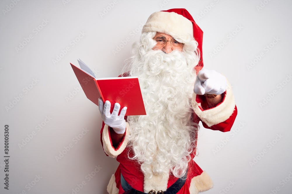 Naklejka premium Middle age man wearing Santa Claus costume reading book over isolated white background pointing displeased and frustrated to the camera, angry and furious with you