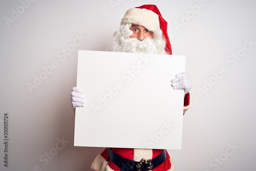 Middle age man wearing Santa Claus costume holding banner over isolated white background scared in shock with a surprise face, afraid and excited with fear expression © Krakenimages.com