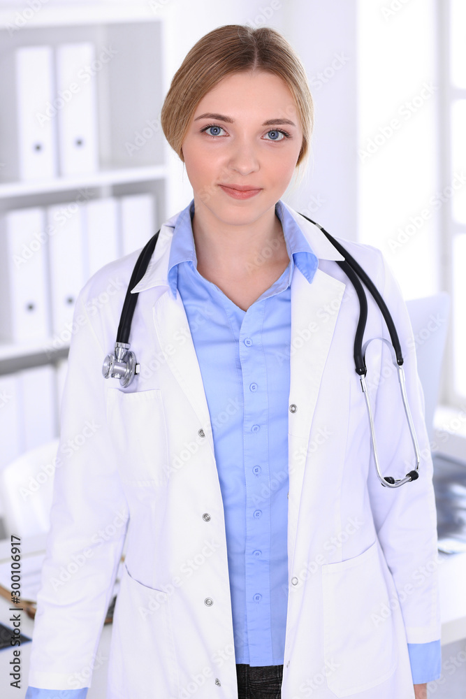 Young woman doctor at work in hospital looking at camera. Blue colored blouse of therapist looks good. Medicine and healthcare concept Young woman doctor at work in hospital looking at camera. Blue colored blouse of therapist looks good. Medicine and healthcare concept