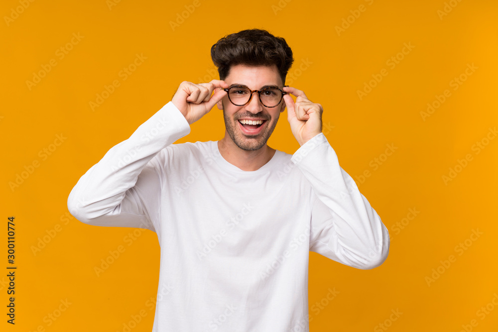 Young man over isolated orange background with glasses and surprised Young man over isolated orange background with glasses and surprised