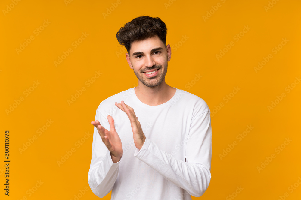 Young man over isolated orange background applauding after presentation in a conference Young man over isolated orange background applauding after presentation in a conference