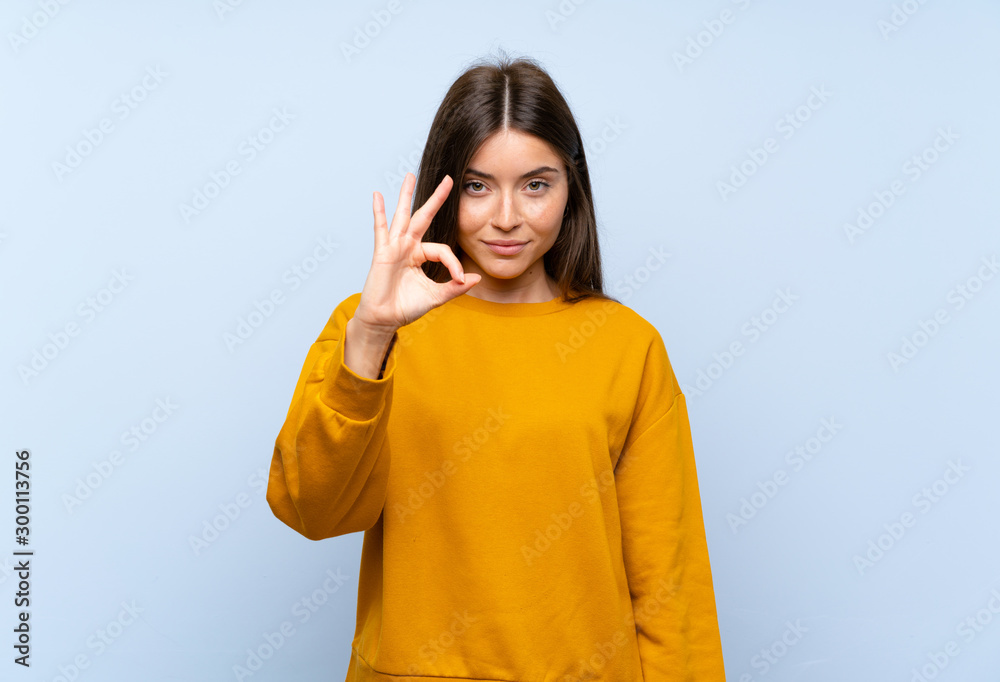 Caucasian young woman over isolated blue wall showing an ok sign with fingers Caucasian young woman over isolated blue wall showing an ok sign with fingers