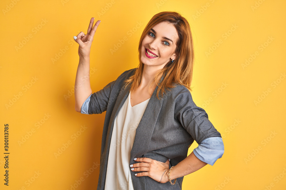 Redhead caucasian business woman over yellow isolated background smiling looking to the camera showing fingers doing victory sign. Number two. Redhead caucasian business woman over yellow isolated background smiling looking to the camera showing fingers doing victory sign. Number two.