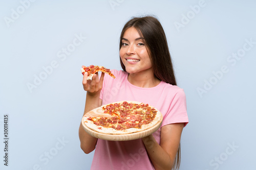 Pretty young girl holding a pizza over isolated blue wall