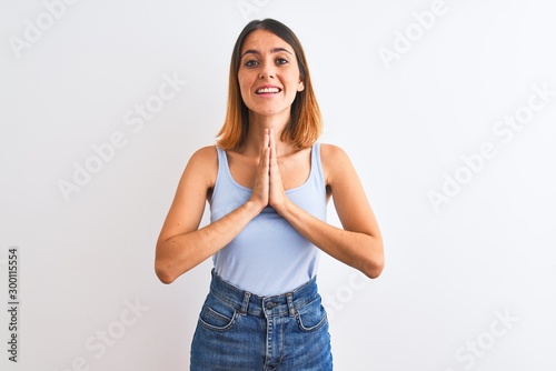 Beautiful redhead woman standing over isolated background praying with hands together asking for forgiveness smiling confident. © Krakenimages.com