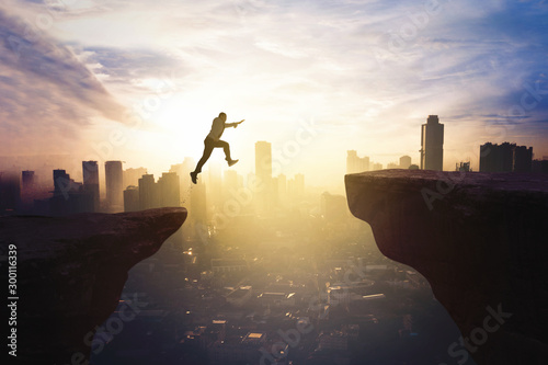 Businessman jumping through gap cliff at sunrise photo