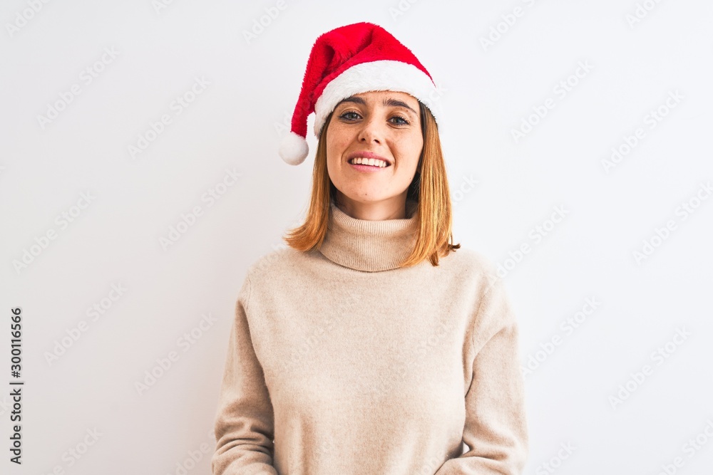 Fototapeta premium Beautiful redhead woman wearing christmas hat over isolated background with hands together and crossed fingers smiling relaxed and cheerful. Success and optimistic
