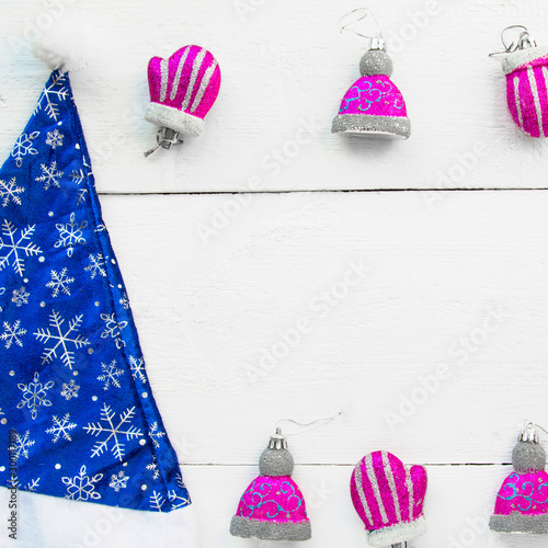 Christmas background top view. Santaclaus blue hat in snowflakes. Pink Christmas toys on a white wooden board background. New Year 2020