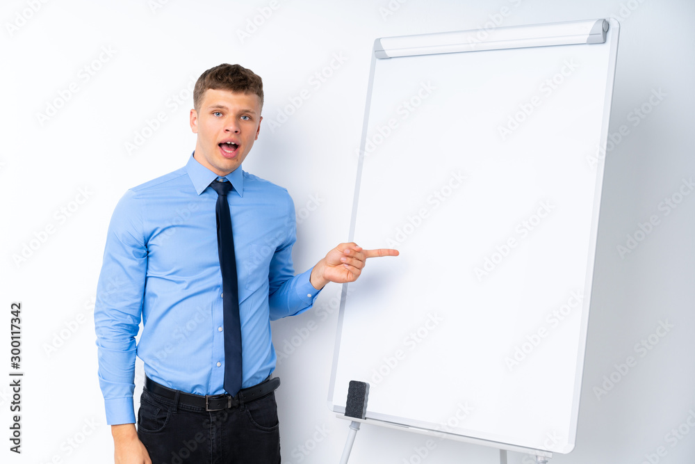 Young businessman giving a presentation on white board surprised and pointing finger to the side Young businessman giving a presentation on white board surprised and pointing finger to the side