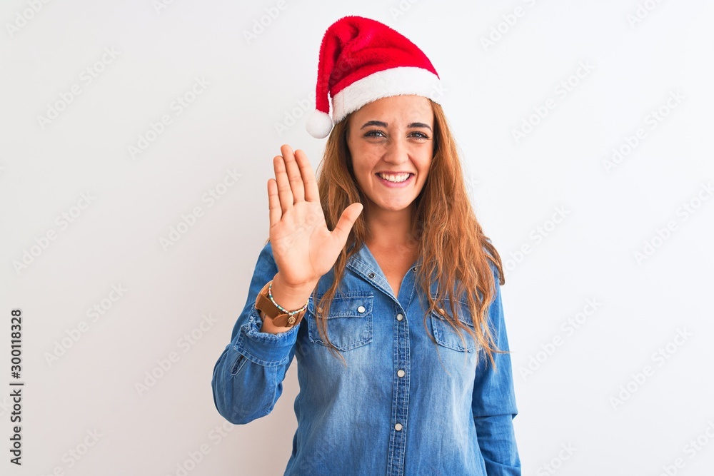 Young beautiful redhead woman wearing christmas hat over isolated background Waiving saying hello happy and smiling, friendly welcome gesture Young beautiful redhead woman wearing christmas hat over isolated background Waiving saying hello happy and smiling, friendly welcome gesture