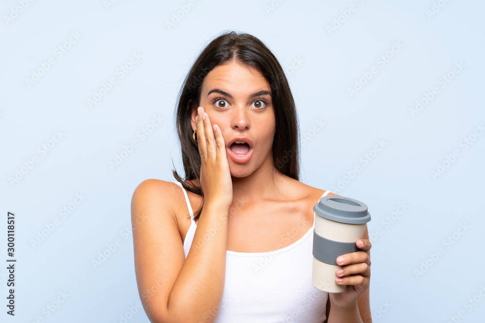 Young woman holding a take away coffee over isolated blue background with surprise and shocked facial expression Young woman holding a take away coffee over isolated blue background with surprise and shocked facial expression