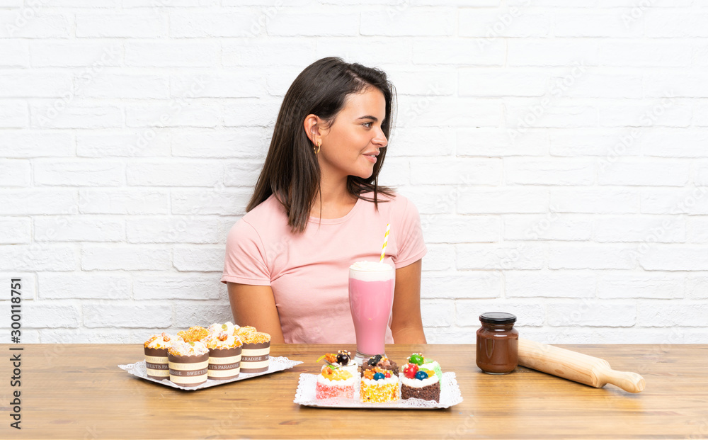 Young girl with lots of different mini cakes looking to the side Young girl with lots of different mini cakes looking to the side