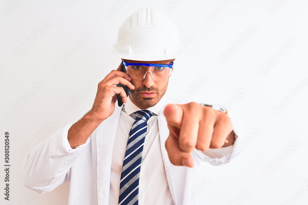 Young scientist man wearing safety helmet and calling using smartphone over isolated background pointing with finger to the camera and to you, hand sign, positive and confident gesture from the front