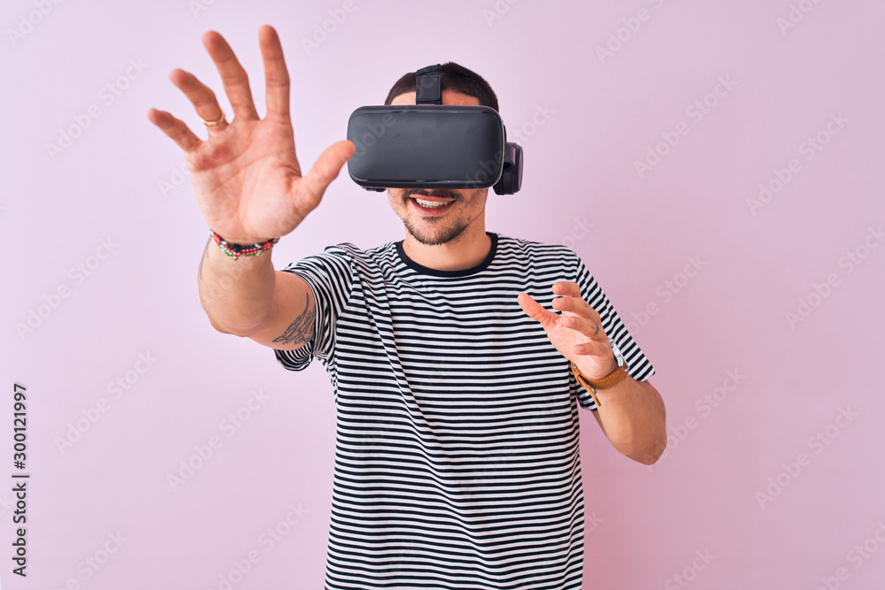 Young man playing video game wearing virtual reality glasses, looking at virtual simulation amazed and smiling happy Young man playing video game wearing virtual reality glasses, looking at virtual simulation amazed and smiling happy