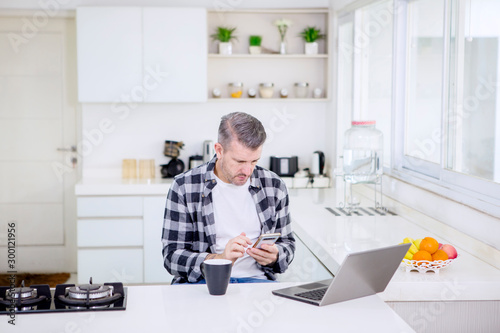 Caucasian man using a phone while works in kitchen