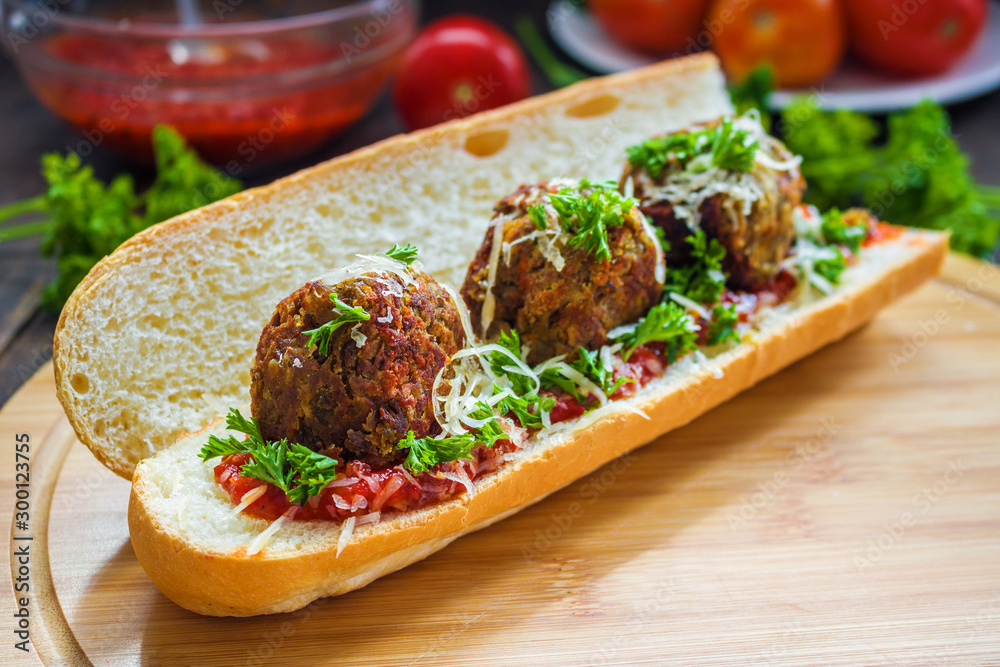 sub sandwich with vegan lentil meatballs tomato sauce grated cheese parsley on cutting board close up sub sandwich with vegan lentil meatballs tomato sauce grated cheese parsley on cutting board close up