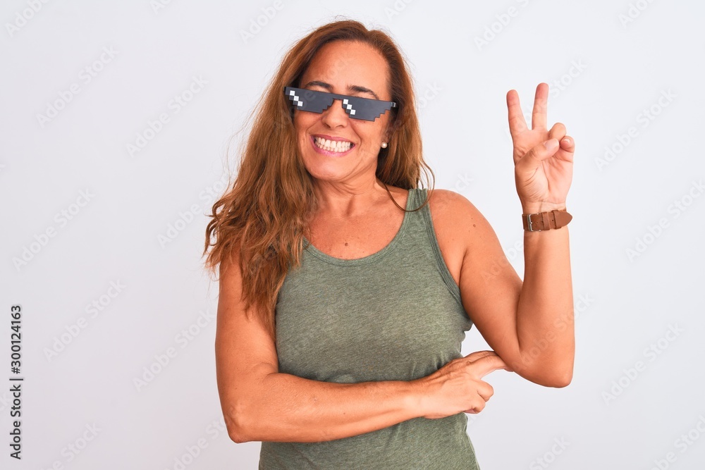 Middle age mature woman wearing thug life sunglasses over isolated background smiling with happy face winking at the camera doing victory sign. Number two. Middle age mature woman wearing thug life sunglasses over isolated background smiling with happy face winking at the camera doing victory sign. Number two.