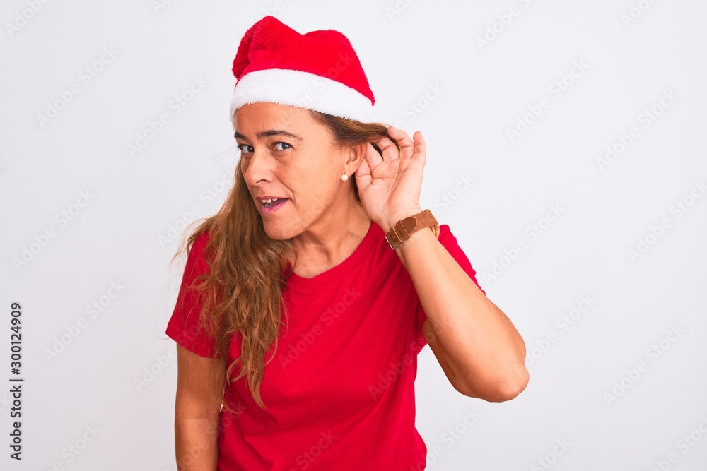 Middle age mature woman wearing christmas hat over isolated background smiling with hand over ear listening an hearing to rumor or gossip. Deafness concept. Middle age mature woman wearing christmas hat over isolated background smiling with hand over ear listening an hearing to rumor or gossip. Deafness concept.