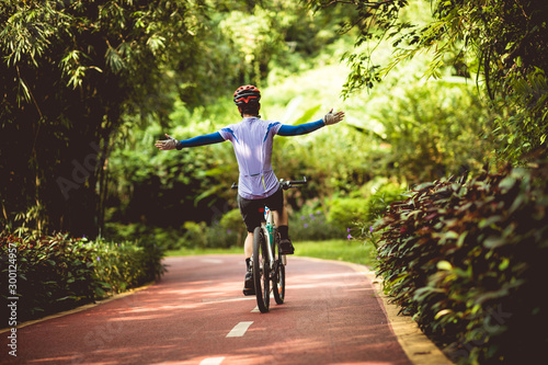 Woman cyclist riding mountain bike on tropical rainforest trail with arms outstretched photo