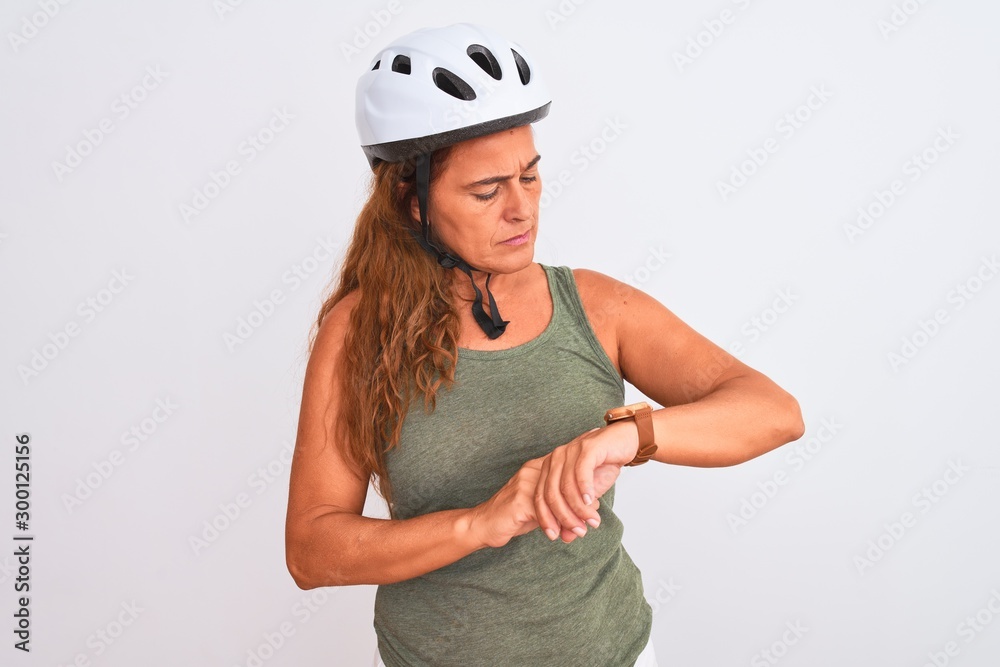 Middle age mature cyclist woman wearing safety helmet over isolated background Checking the time on wrist watch, relaxed and confident Middle age mature cyclist woman wearing safety helmet over isolated background Checking the time on wrist watch, relaxed and confident