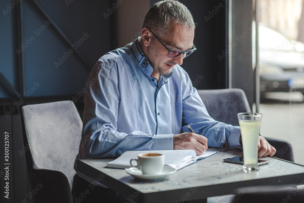 Smiling businessman writing in a notebook at cafe. Smiling businessman writing in a notebook at cafe.