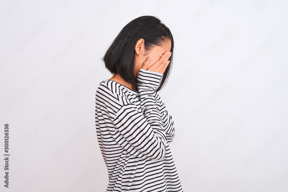 Young chinese woman wearing striped t-shirt standing over isolated white background with sad expression covering face with hands while crying. Depression concept. Young chinese woman wearing striped t-shirt standing over isolated white background with sad expression covering face with hands while crying. Depression concept.
