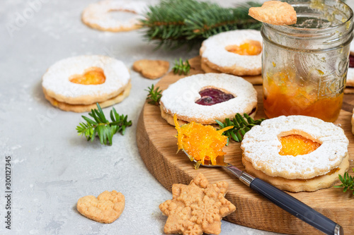 Jelly Christmas Linzer cookies with orange and red jam on a wooden board with festive decoration. Shortcrust pastry. 