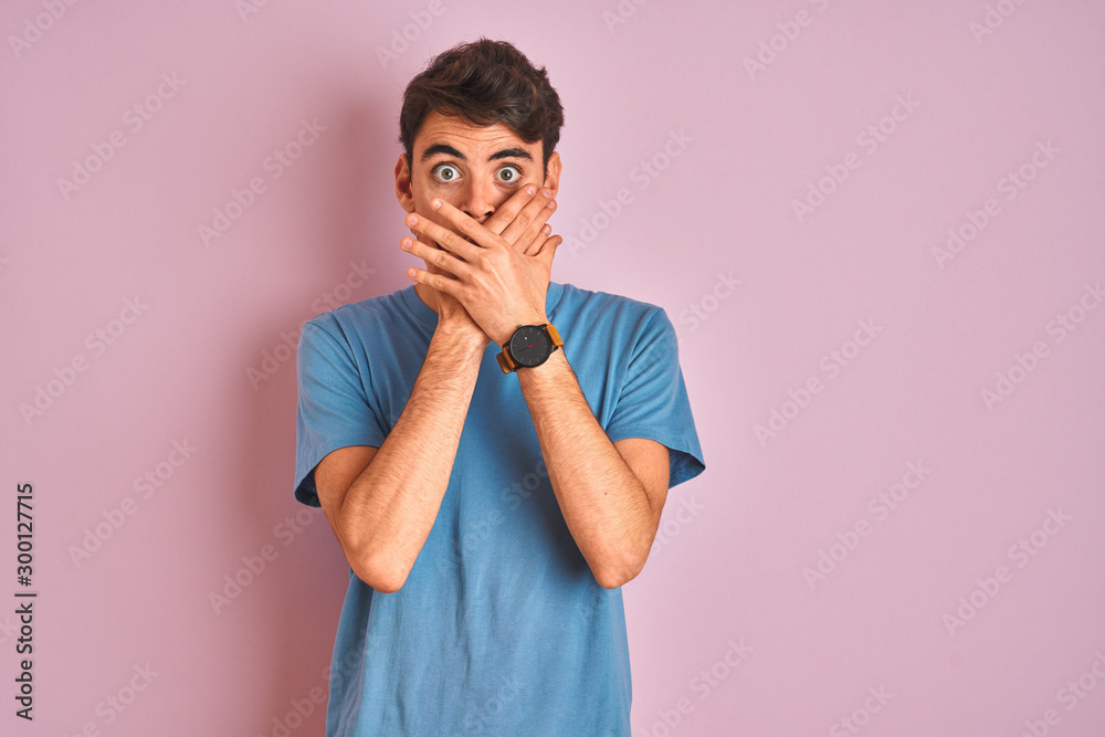 Teenager boy wearing casual t-shirt standing over blue isolated background shocked covering mouth with hands for mistake. Secret concept. Teenager boy wearing casual t-shirt standing over blue isolated background shocked covering mouth with hands for mistake. Secret concept.