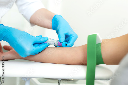a gloved nurse inserts a needle into a vein on the patient’s arm and draws blood into a vacuum container. Blood sampling procedure