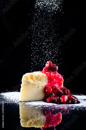 cherry cheesecake on a black background with reflection and flying icing sugar photo