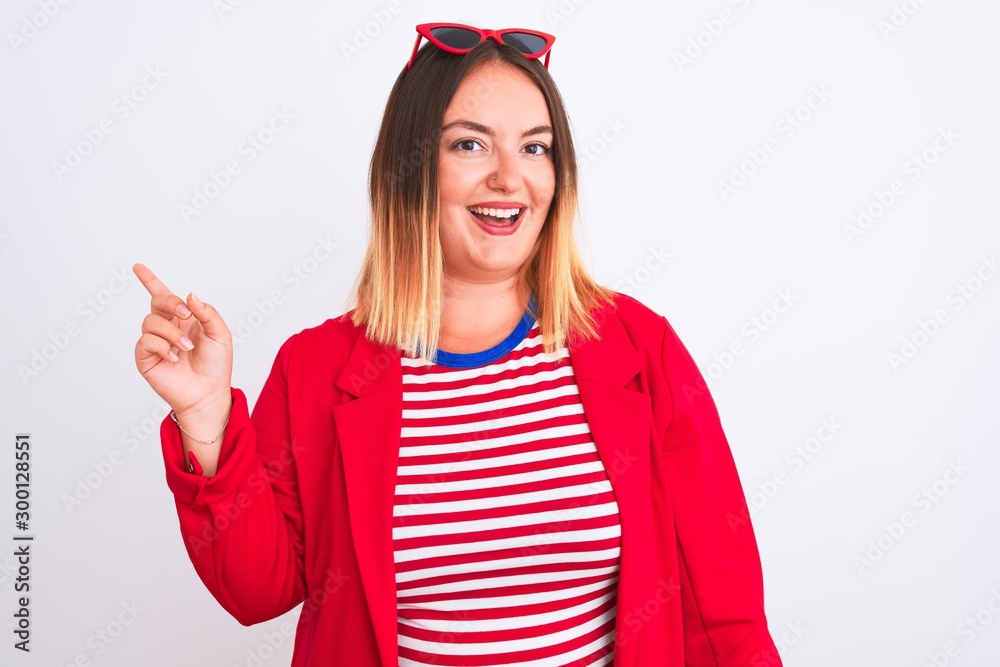 Young beautiful woman wearing striped t-shirt and jacket over isolated white background with a big smile on face, pointing with hand and finger to the side looking at the camera. Young beautiful woman wearing striped t-shirt and jacket over isolated white background with a big smile on face, pointing with hand and finger to the side looking at the camera.
