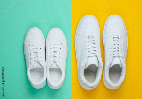 Two pairs of white sneakers on a two-color paper background. Top view