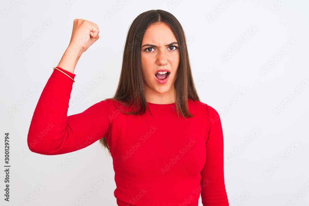 Young beautiful girl wearing red casual t-shirt standing over isolated white background angry and mad raising fist frustrated and furious while shouting with anger. Rage and aggressive concept.