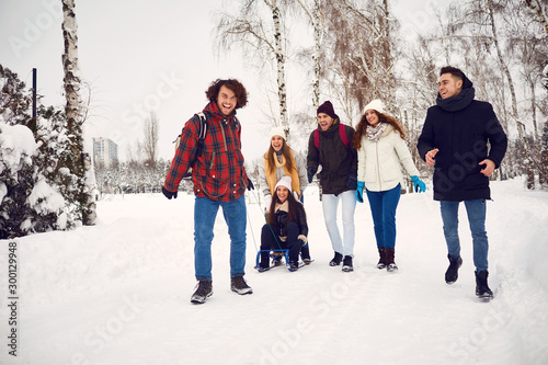 Group of friends enjoying pulling a sled in the snow in winter