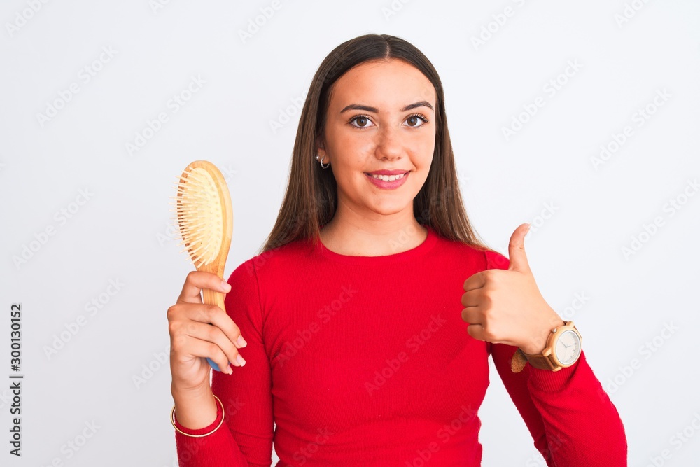 Young beautiful girl holding hair comb standing over isolated white background happy with big smile doing ok sign, thumb up with fingers, excellent sign Young beautiful girl holding hair comb standing over isolated white background happy with big smile doing ok sign, thumb up with fingers, excellent sign