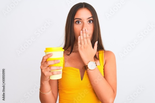 Young beautiful girl drinking paper glass of take away coffee over isolated white background cover mouth with hand shocked with shame for mistake, expression of fear, scared in silence, secret concept