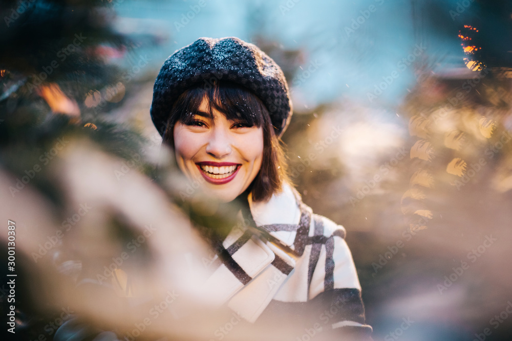 Close up photo of young brunette next to branches of spruce with garland in evening Close up photo of young brunette next to branches of spruce with garland in evening