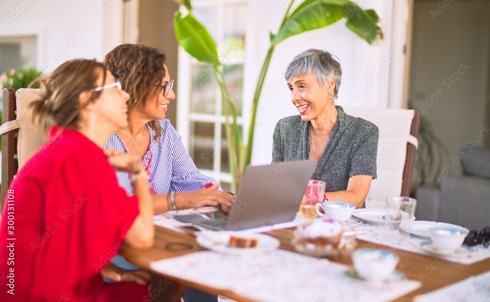 Meeting of middle age women having lunch and drinking coffee. Mature friends smiling happy using laptop at home on a sunny day Meeting of middle age women having lunch and drinking coffee. Mature friends smiling happy using laptop at home on a sunny day