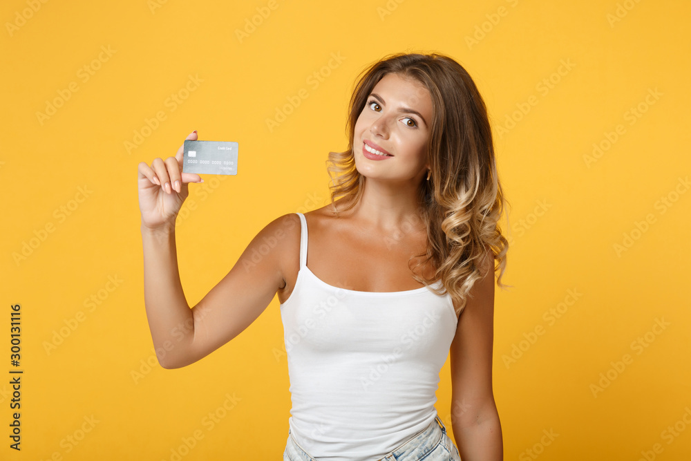 Pretty smiling young woman girl in light casual clothes posing isolated on yellow orange wall background, studio portrait. People lifestyle concept. Mock up copy space. Hold in hand credit bank card. Pretty smiling young woman girl in light casual clothes posing isolated on yellow orange wall background, studio portrait. People lifestyle concept. Mock up copy space. Hold in hand credit bank card.
