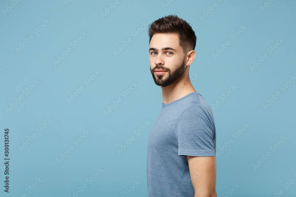 Side view of young attractive man in casual clothes posing isolated on blue wall background studio portrait. People sincere emotions lifestyle concept. Mock up copy space. Standing and looking camera. Side view of young attractive man in casual clothes posing isolated on blue wall background studio portrait. People sincere emotions lifestyle concept. Mock up copy space. Standing and looking camera.