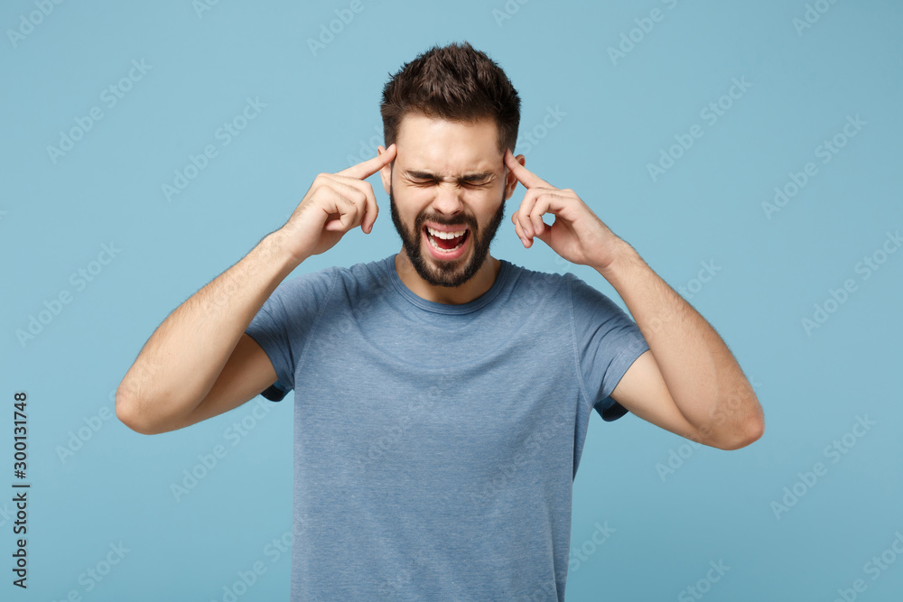 Young crazy man in casual clothes posing isolated on blue wall background, studio portrait. People lifestyle concept. Mock up copy space. Screaming, keeping eyes closed, holding index fingers on head. Young crazy man in casual clothes posing isolated on blue wall background, studio portrait. People lifestyle concept. Mock up copy space. Screaming, keeping eyes closed, holding index fingers on head.