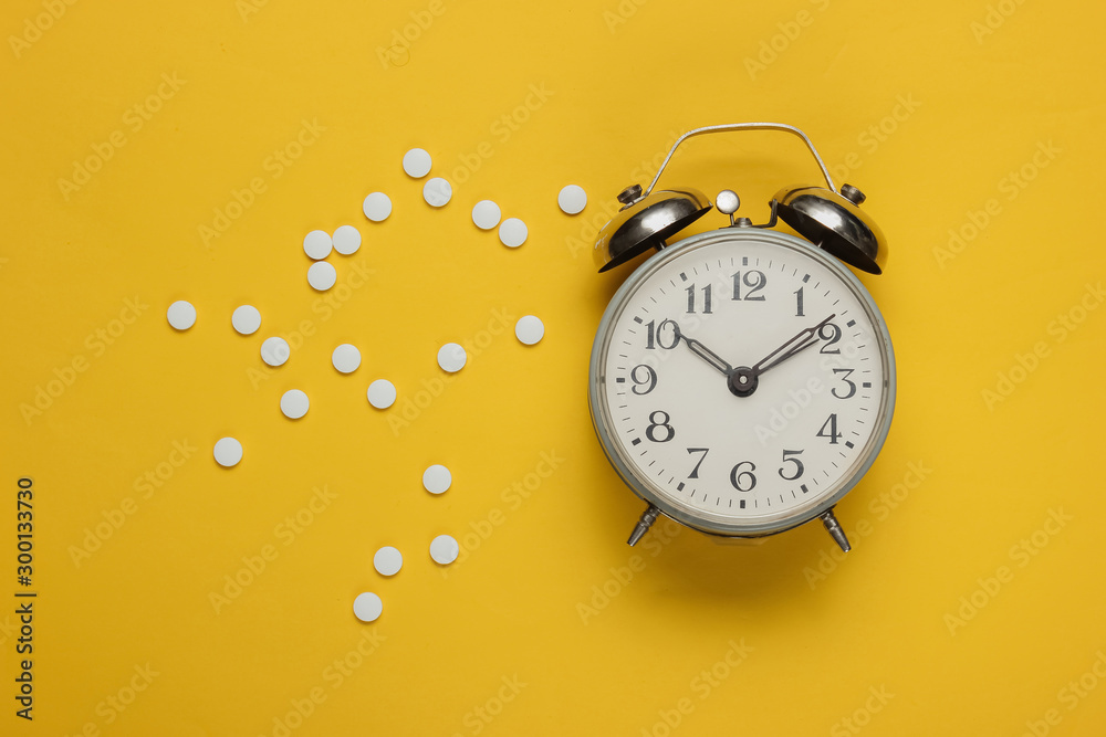 Time to take pills. Pills and alarm clock on yellow background. Top view - obrazy, fototapety, plakaty 