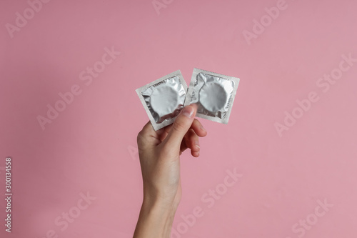 Female hand holding condom on pink background. Top view. The concept of sexual preservation