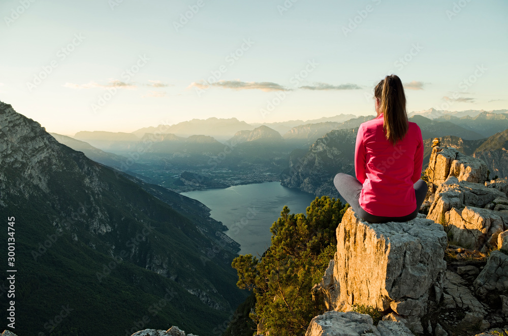 Naklejka premium Young woman sitting in front of a beautiful landscape, thinking and meditating at sunrise