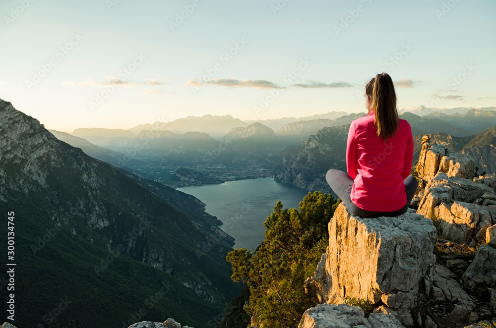 Young woman sitting in front of a beautiful landscape, thinking and meditating at sunrise