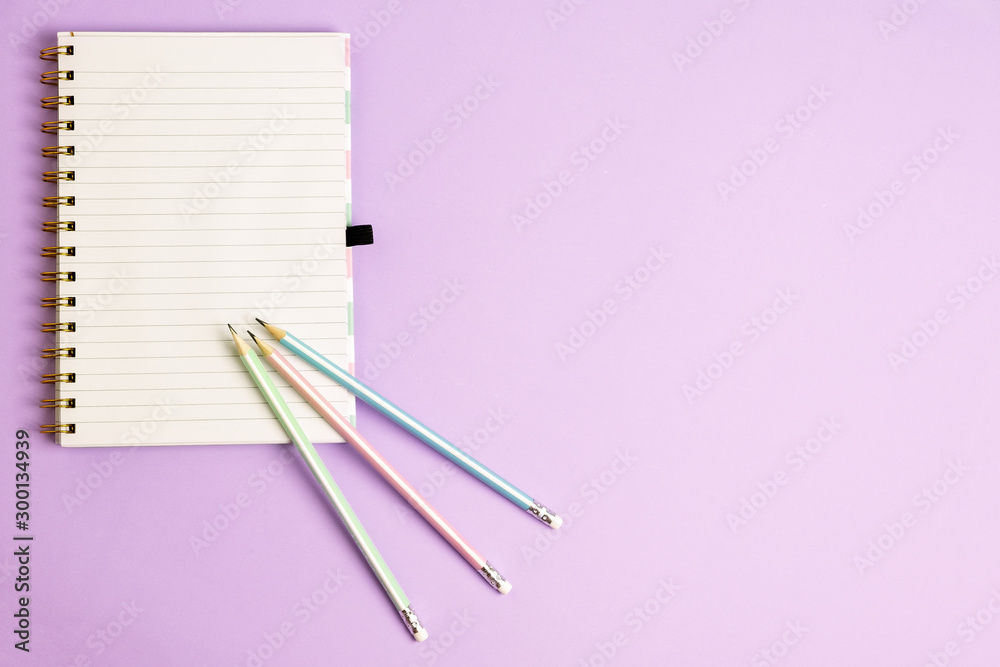 Top view of blank notebook with pencils on purple pastel background with copy space Top view of blank notebook with pencils on purple pastel background with copy space