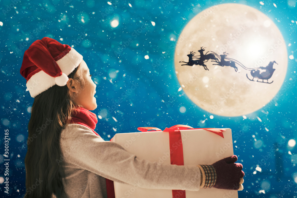 Cute little girl with christmas presents. Santa Claus flying in moon sky Cute little girl with christmas presents. Santa Claus flying in moon sky