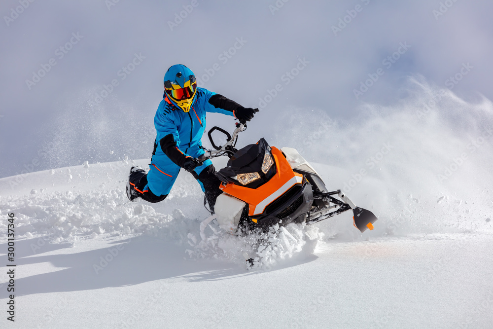 the guy turns a snowmobile in a mountain valley on the background of the clear snow and sky, leaving behind a trail of splashes. bright snow bike and suit without brands. Boondocker sports snowmobile